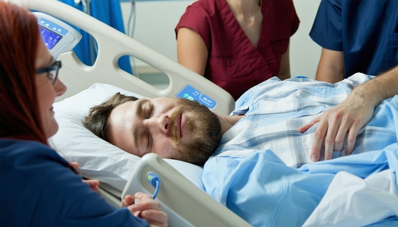 someone asleep in a hospital bed with family around them